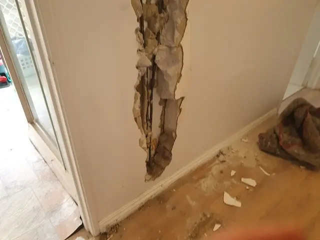 Drywall broken open at a doorway with plaster dust and debris scattered across the floor