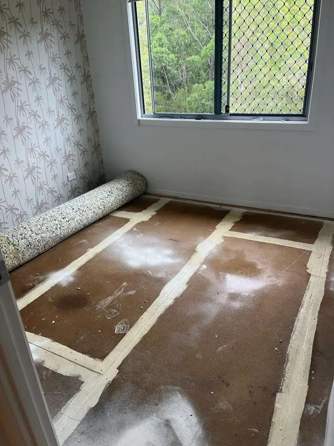 A bedroom with the carpet rolled back so the tack strip and bare floor show
