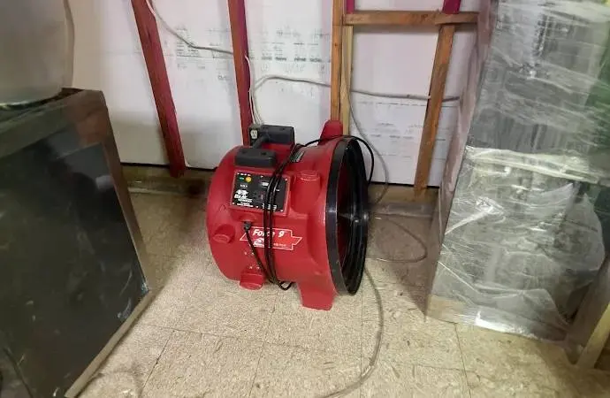 Red air mover drying a room with the lower wall opened and plastic sheeting hung, the drying stage after mud is removed