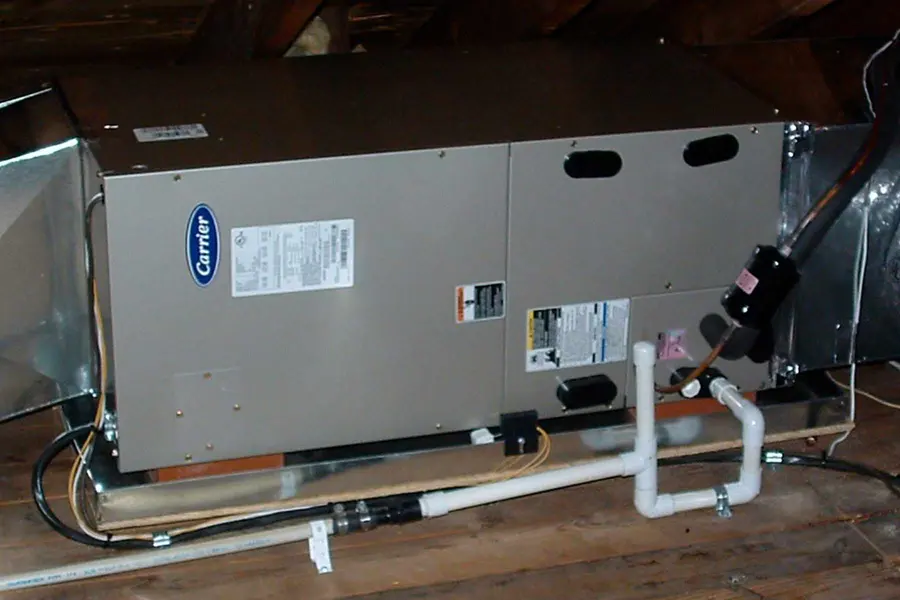 Attic air handler with white PVC condensate drain lines on a wood platform