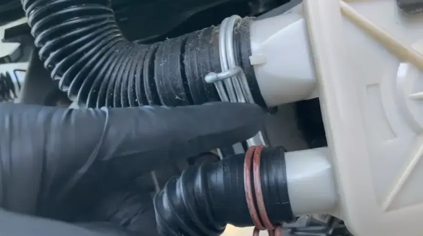 Gloved hand checking the drain hose connections on a washing machine