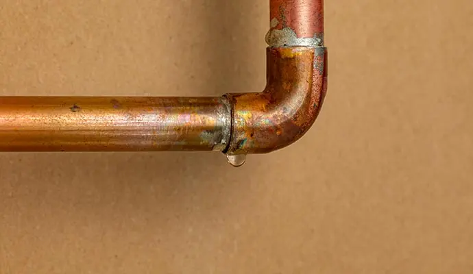 Corroded copper pipe elbow with water dripping from the joint