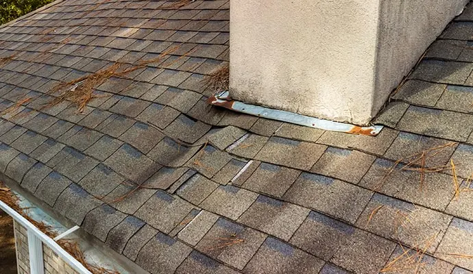 Shingle roof with lifted shingles around the flashing at a stucco chimney
