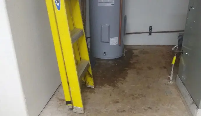 Water heater in a utility closet with leaked water spread across the floor